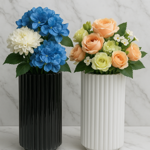 odern ribbed ceramic vases in black and white with faux floral arrangements, featuring blue hydrangeas and white dahlias in one vase and peach roses with green accents in the other, styled on a marble background.